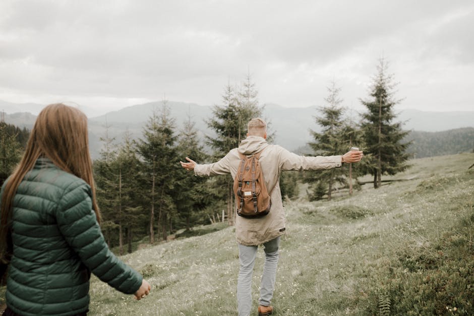 Couple exploring a scenic mountain landscape with lush greenery on an overcast day.