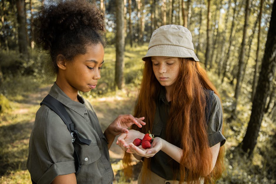 Two girls in the forest holding strawberries, enjoying a summer adventure.